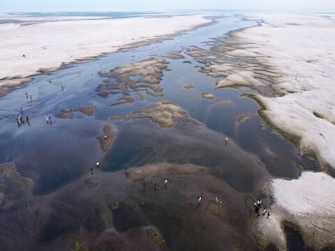 Aerial view of people walking across a vast dry riverbed with shallow water channels and sandy banks in Bogura, Rajshahi Division, Bangladesh.
