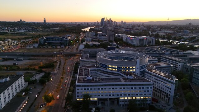Aerial view of a large circular office complex with modern architecture surrounded by roads and urban infrastructure at sunset in Offenbach am Main, Hessen, Germany.