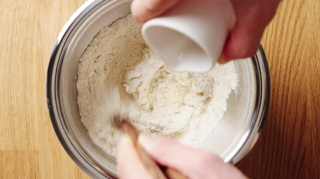 Chopsticks mix flour and water into noodle dough in bowl on wooden table. Noodle dough rests for smooth texture and elastic gluten. Stretch noodle dough for soup, stir-fry, ramen, curry or salads.