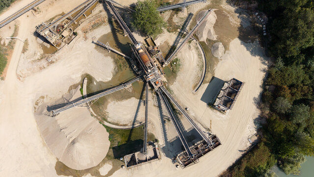 Aerial view of the Manara Fratelli and C. gravel extraction site with conveyor belts, industrial machinery, and piles of sand and gravel in Peschiera Borromeo, Lombardia, Italy.
