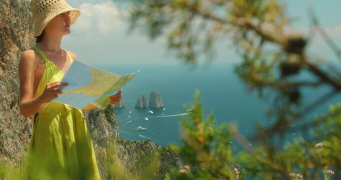 Woman reads a map on a cliffside overlooking sea and Faraglioni rock formations on Capri Italy