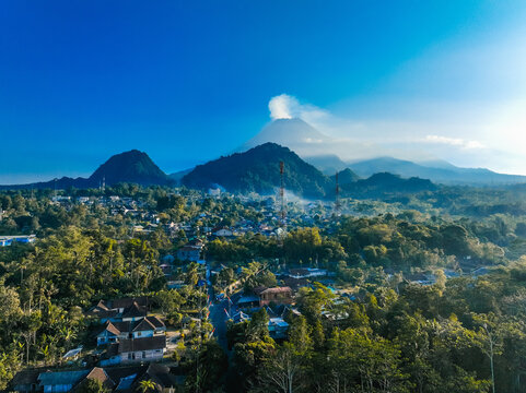 Aerial view of Kaliurang town at the foot of Mount Merapi, with lush forests, traditional houses, and clear blue skies in Kecamatan Pakem, Daerah Istimewa Yogya, Indonesia.