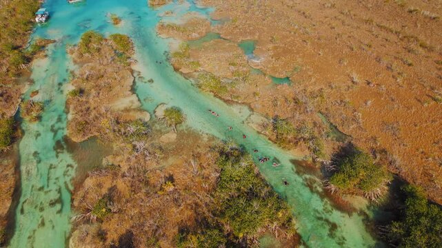 People floating through narrow turquoise canal of Bacalar lagoon in Mexico
