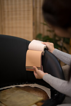 Hands of furniture designer selecting beige leather fabric swatch comparing materials in modern design studio workspace