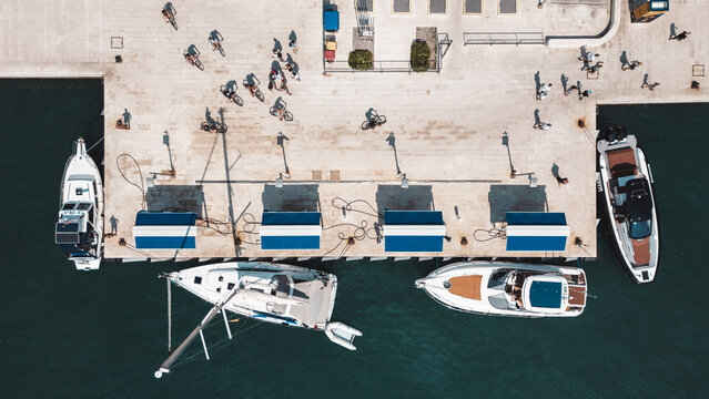 Aerial view of boats docked at a pier in Split with people walking along the stone promenade and blue water, Split, Split-Dalmatia County, Croatia.