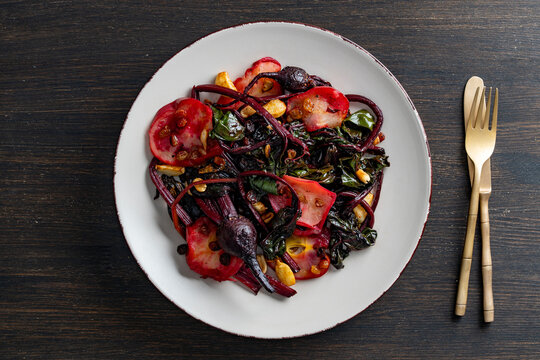 Roasted beetroot salad with chard stems and raisins. Healthy warm salad with roasted whole beetroots leafy chard stems and golden raisins on white plate with golden cutlery over wooden background