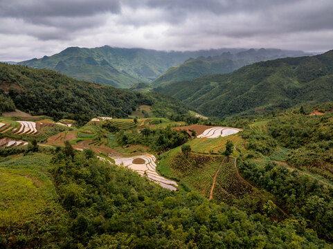 Aerial view of the Ha Giang Loop featuring lush green terraced rice fields, rolling mountains, and cloudy skies in Dong Van, Tuyen Quang, Vietnam.