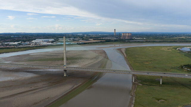 Aerial view of the Mersey Gateway Bridge spanning the River Mersey, with industrial buildings and power station cooling towers in the background in Runcorn, United Kingdom.