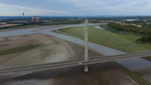 Aerial view of the Mersey Gateway Bridge spanning the River Mersey with mudflats and industrial cooling towers in the distance in Runcorn, United Kingdom.