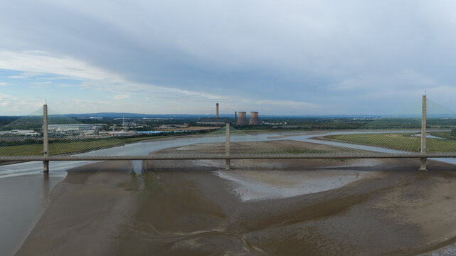 Aerial view of Mersey Gateway Bridge spanning the River Mersey with mudflats and industrial cooling towers in the background under a cloudy sky Runcorn, United Kingdom.