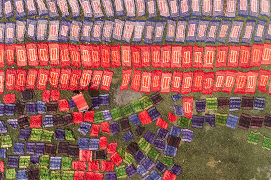 Aerial view of colorful fabrics laid out on the grass to dry in a textile dyeing facility in Narayanganj, Dhaka, Bangladesh.