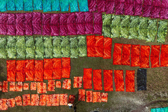 Aerial view of vibrant tie-dye fabrics laid out to dry on the ground in a textile facility in Narayanganj, Dhaka, Bangladesh.