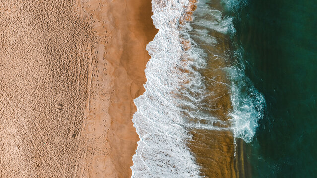 Aerial view of the sandy beach and turquoise waves crashing on the shore in Nazare, Leiria District, Portugal.