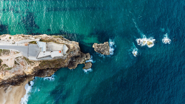 Aerial view of the historic Forte de Sao Miguel Arcanjo lighthouse perched on a rugged cliff overlooking the Atlantic Ocean in Nazare, Leiria District, Portugal.
