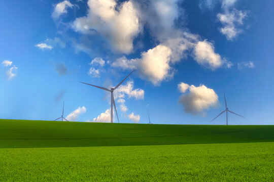 Wind turbines across a vibrant green field under a blue sky with soft clouds, representing renewable energy, clean power, sustainability, environmental conservation, and a green future