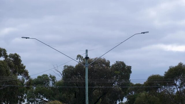 A double-arm metal streetlight pole featuring light fixtures extending over overhead power lines in Melbourne, Australia.Concepts of public lighting and urban road infrastructure.