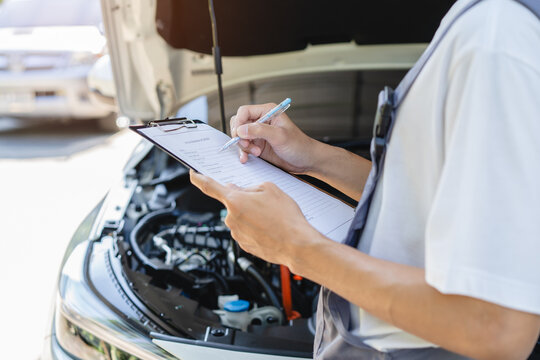 Auto check up and car service shop concept. Mechanic writing job checklist to clipboard to estimate repair quotation to client at workshop garage.