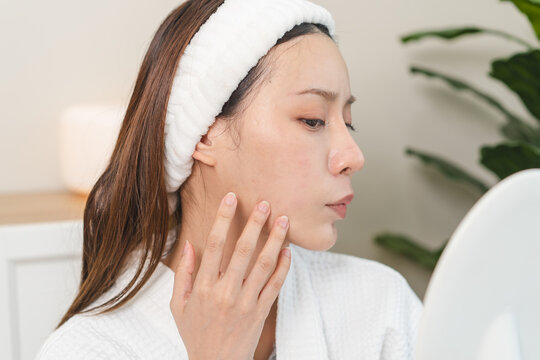 An Asian young woman looking at the mirror and feeling worried about her facial skin problem that cracked and aging.