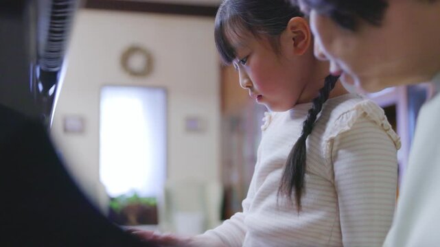 女性の先生とピアノの鍵盤を見つめて練習する女の子