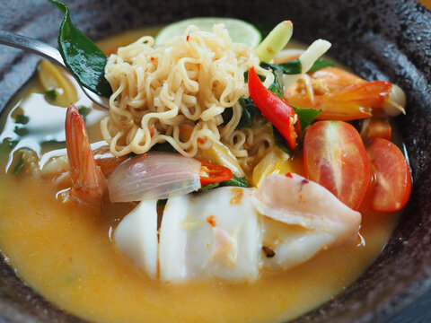The tom yum instant noodles in the bowl contain shrimp and squid. It looks delicious and appetizing.