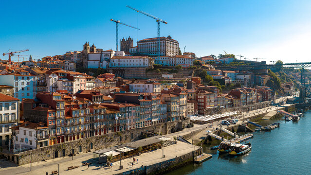 Aerial view of the historic Ribeira district with colorful buildings, the Douro River waterfront, and construction cranes under a clear blue sky in Porto, Porto District, Portugal.