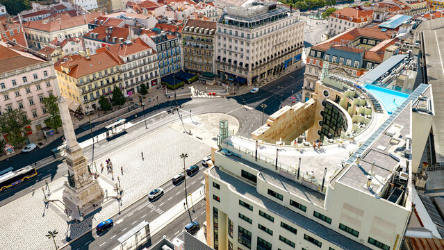 Aerial view of Rossio Square with its central obelisk, historic architecture, busy streets, and a rooftop pool in Lisbon, Lisbon, Portugal.