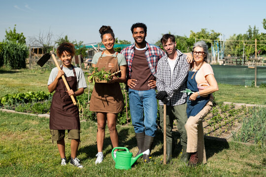 Group of smiling diverse people holding gardening tools in a community garden