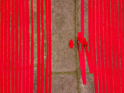 Aerial view of vibrant red fabric strips laid out to dry on a stone surface in Narsingdi, Dhaka Division, Bangladesh.