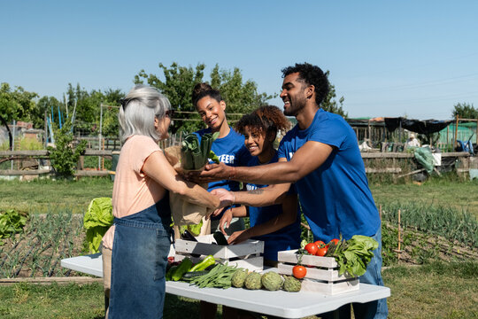 Group of volunteers giving a bag of fresh produce to an elderly woman at a community garden