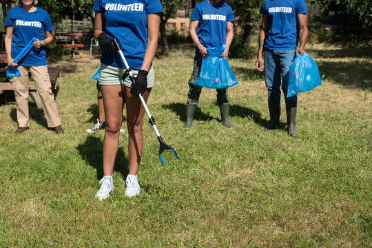 Group of volunteers collecting garbage in blue bags and using grabbers for a clean environment