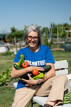 Woman volunteer smiling, holding freshly harvested organic vegetables from a community garden