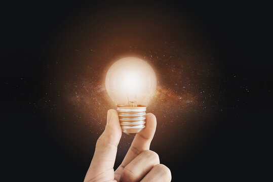 Hand holding bright light bulb, with stars. Imagination, innovative, ideas and futuristic concepts