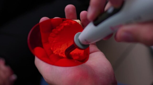 Hands using rotary tool to sand inner rim of glossy red plastic cup, with visible rotation, contact, and material removal during careful shaping in close overhead view