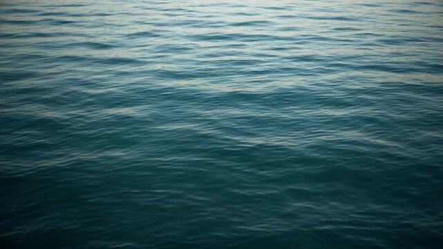 Gently rippling sea water, showing smooth wave textures transitioning from deep turquoise in the foreground to soft light blue reflections near the horizon under natural daylight. 4K.