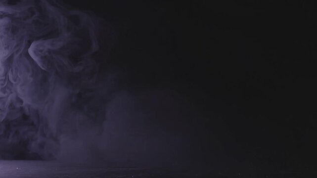 Billowing purple smoke moving across a dark surface, creating a mysterious and abstract background with thick clouds of mist, vapor, and fog for a spooky atmospheric effect