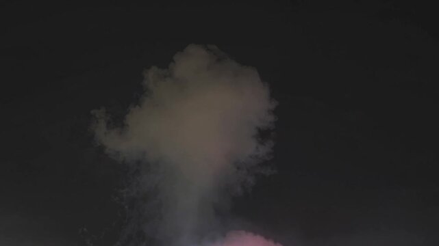 Colorful pyrotechnic firework explosion creating a dense cloud of smoke against the dark night sky during a festival or celebration event, illuminating the darkness