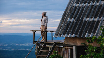 Fototapeta premium A woman standing on wooden balcony, looking at mountain views on cloudy morning