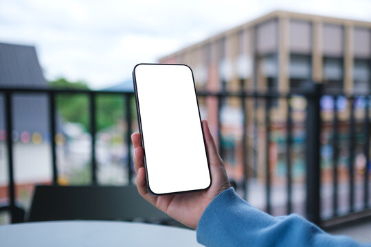 Mockup image of a woman holding and using mobile phone with blank desktop screen in cafe