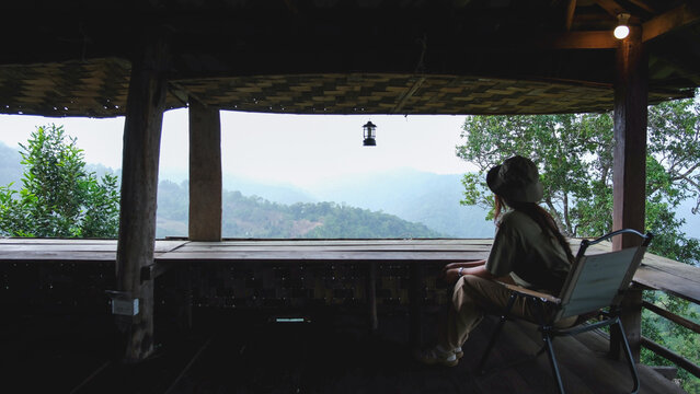 Rear view of a woman sitting on wooden balcony and looking at mountain views
