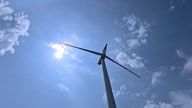 Wind turbine blades spinning against a sunny blue sky