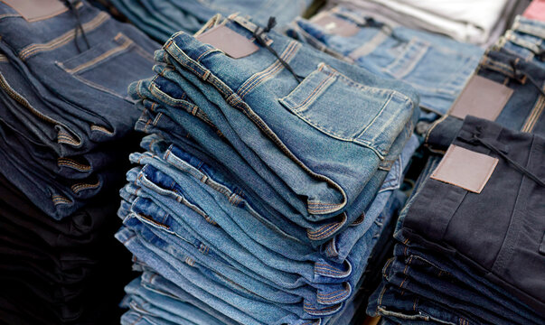 Stacks of blue jeans in various shades, showcasing denim texture, stitching, pockets, fashion apparel, retail, and shopping concepts