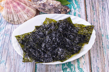 Crispy nori seaweed sheets on white plate with seashells on rustic wooden background © Andrei Starostin