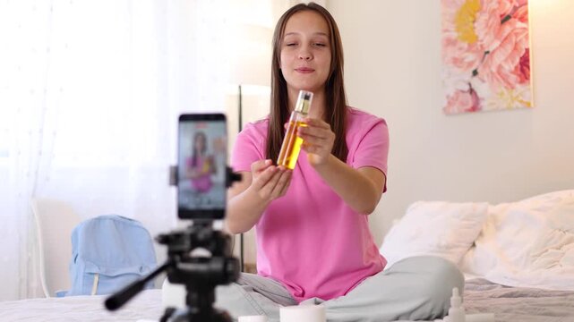 Teenage girl filming beauty blog at home while reviewing skincare product for social media audience. 