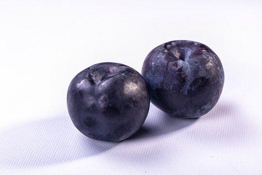 Two fresh ripe plums on white textured background
