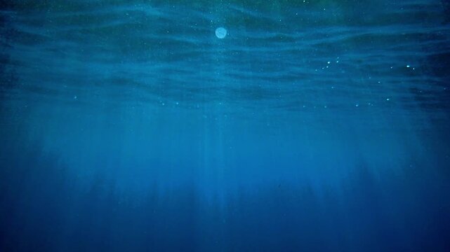 Dark blue ocean surface seen from underwater. Sunlight rays under water. Underwater blue background in sea bottom. Sunbeam and ripples. wave lights. Slow motion. Mediterranean sea. Real video water.