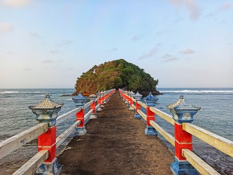 Aerial view of Jembatan Panjang Beach in East Java, Indonesia, featuring a colorful bridge over the ocean leading to a lush tropical island, scenic coastal tourism destination.