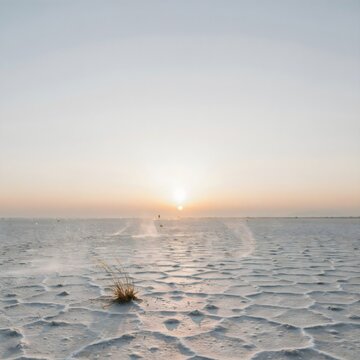 Paisaje minimalista de un salar des&eacute;rtico con patrones hexagonales de sal y un atardecer en el horizonte