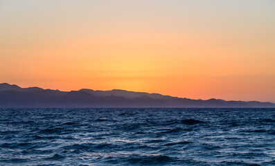 Fototapeta premium Majestic sunset over tranquil ocean waves and distant mountains near the shore