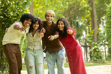 Fototapeta premium Group of diverse indian asian Gen z young adult friends laughing and embracing each other outdoors, sharing a happy moment and representing youth, unity, and friendship in a summer park. .