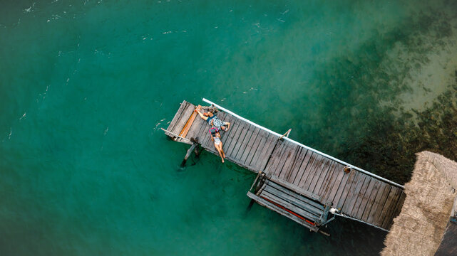 Top aerial view of couple tourist in happiness and relax moment on wooden pier, enjoy the summer trip in tropical island
